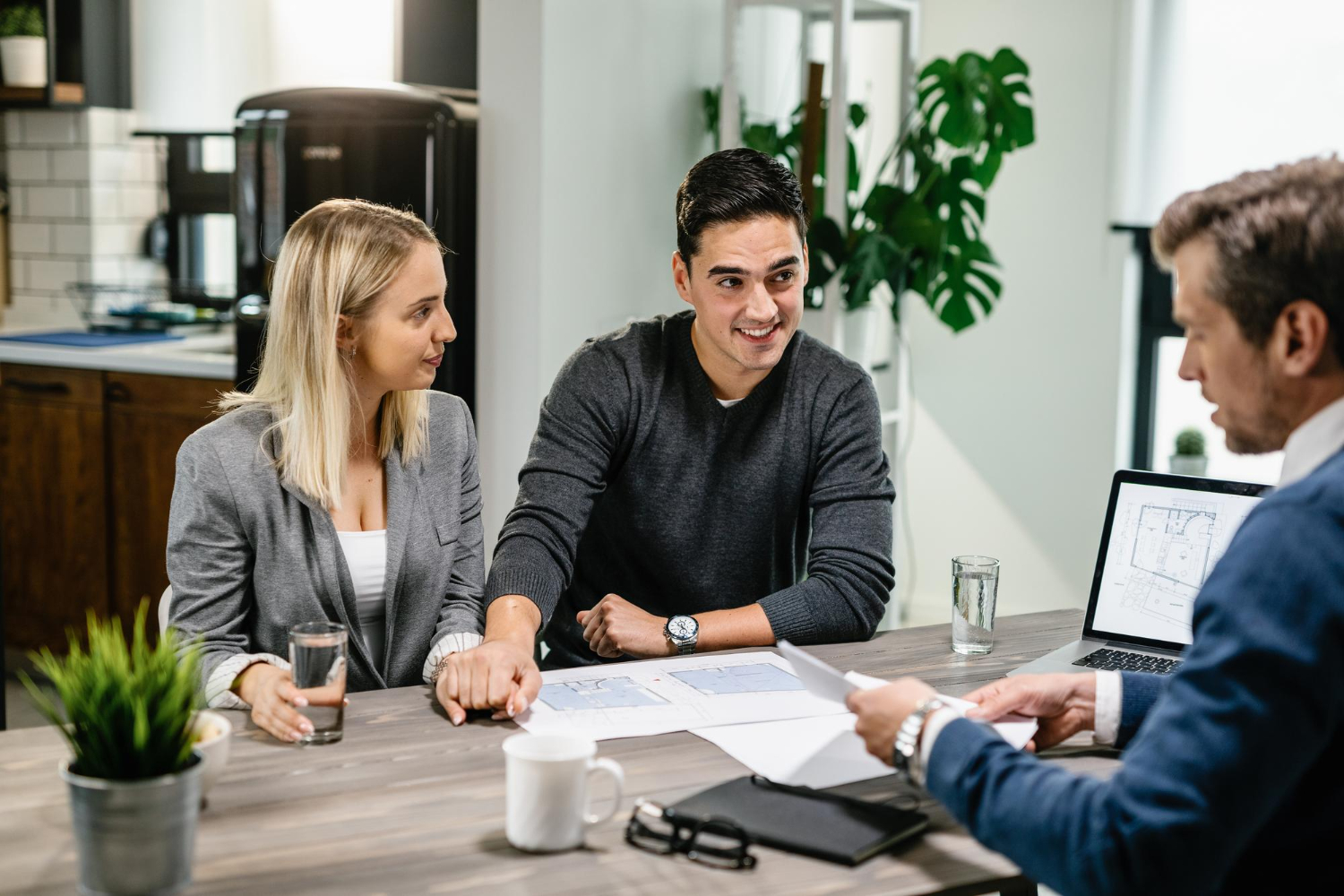 A Young Couple Sitting Across A Desk From A Professional Advisor In A Modern Office, Reviewing Documents And Smiling During A Consultation